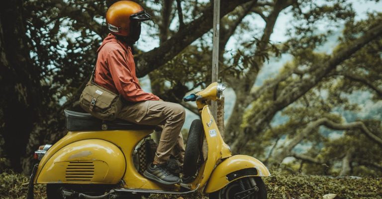 A man riding a vintage yellow Vespa scooter through a lush forest in East Java, Indonesia.